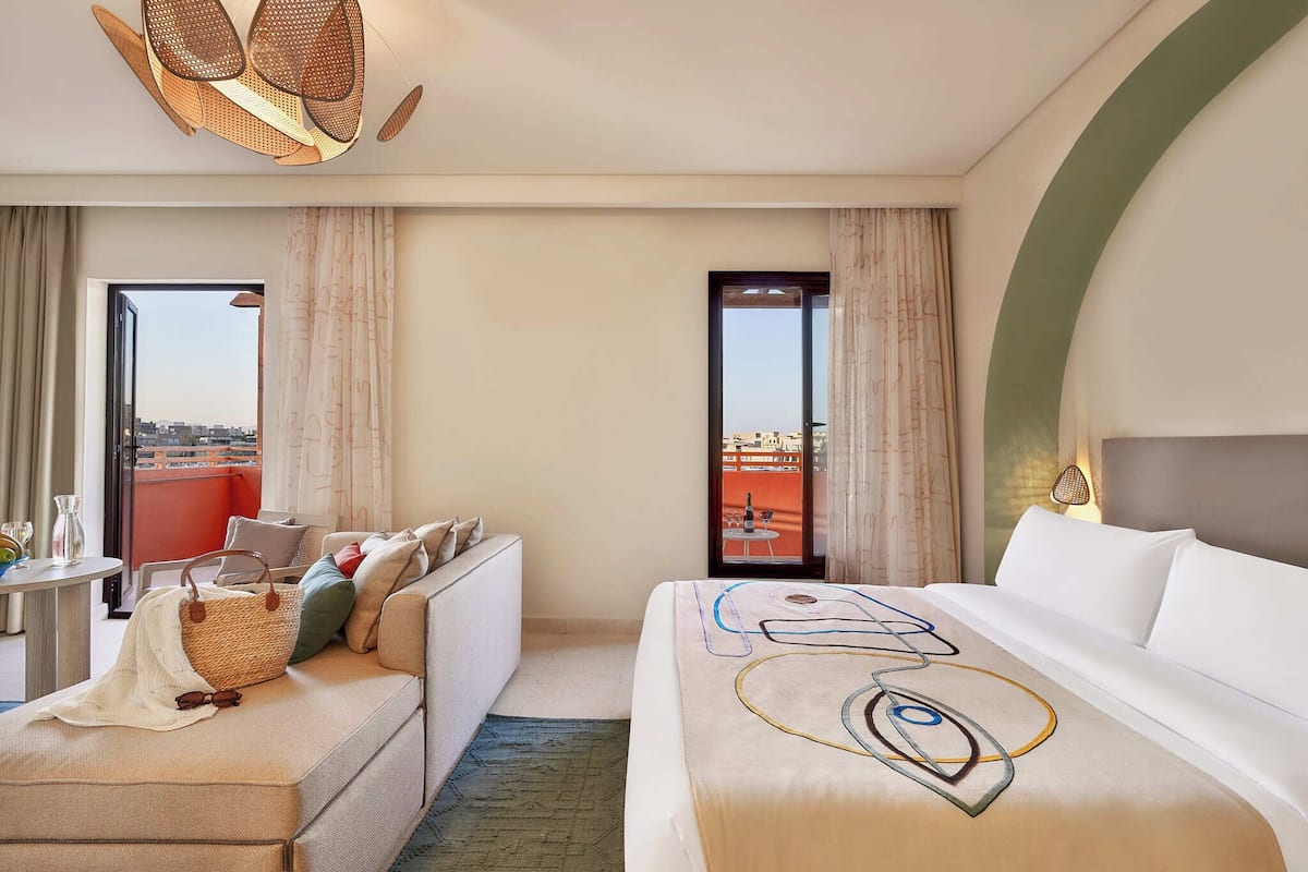 Een hotelkamer met een bed, een bank, een kleine tafel en uitzicht op de stad.