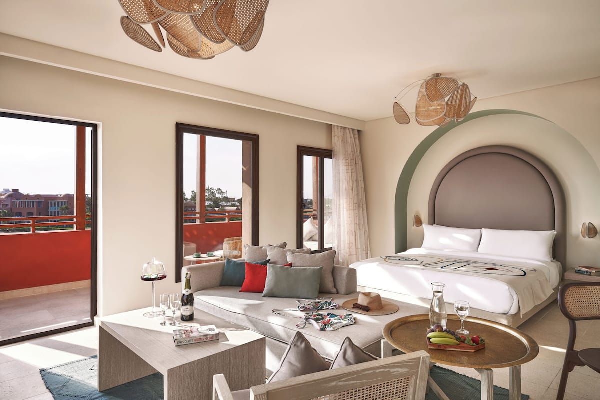 Een moderne hotelkamer met een groot bed, een sofa, een eettafel en een balkon met uitzicht op de stad.