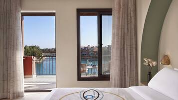 A hotel room with a bed, a view of a balcony with outdoor furniture, and a vase with flowers.