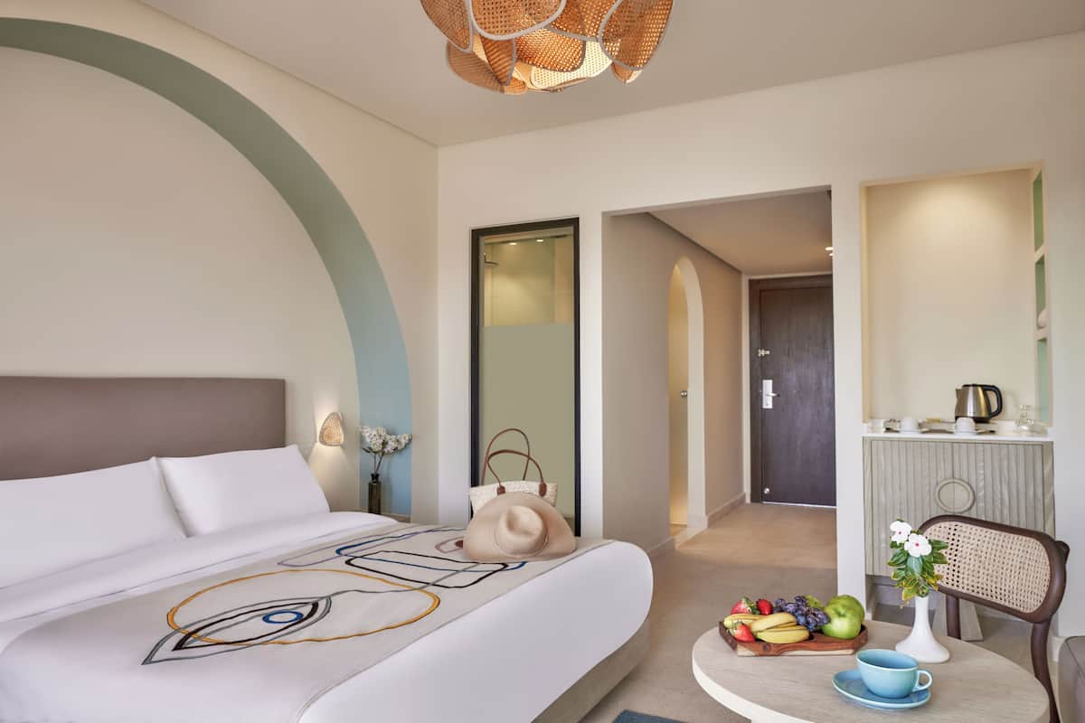 Een moderne hotelkamer met een groot bed, een zithoek met fruit en een kopje, en een kitchenette.