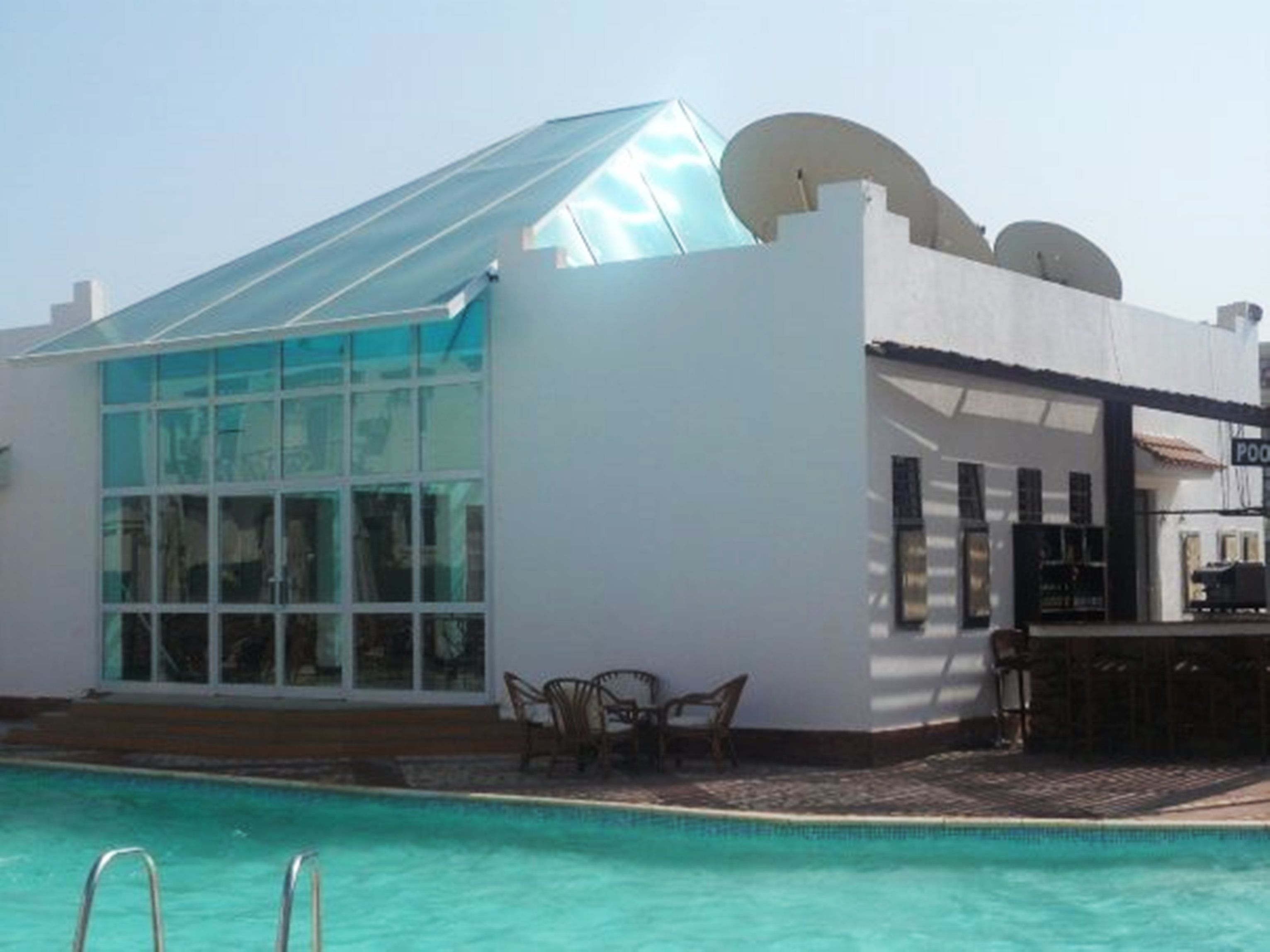 Un área junto a la piscina con una estructura de vidrio, mobiliario exterior y una zona de bar.