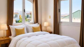 Una habitació d'hotel amb un llit gran, dues taules de nit amb làmpades i grans finestres amb cortines.
