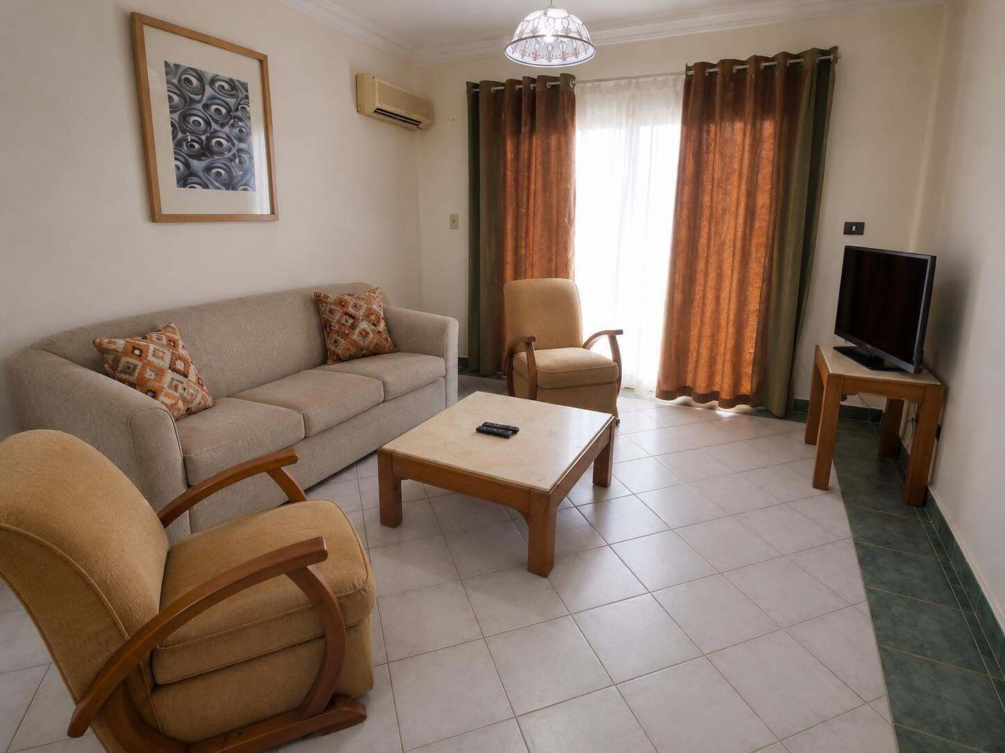 Uma sala de estar com sofá, duas poltronas, mesa de centro, televisão em um móvel e um quadro na parede.