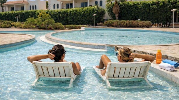 A swimming pool with two lounge chairs, a clear sky, and a building with a tiled roof in the background. - Logaina Sharm Resort (Sharm El Sheikh)