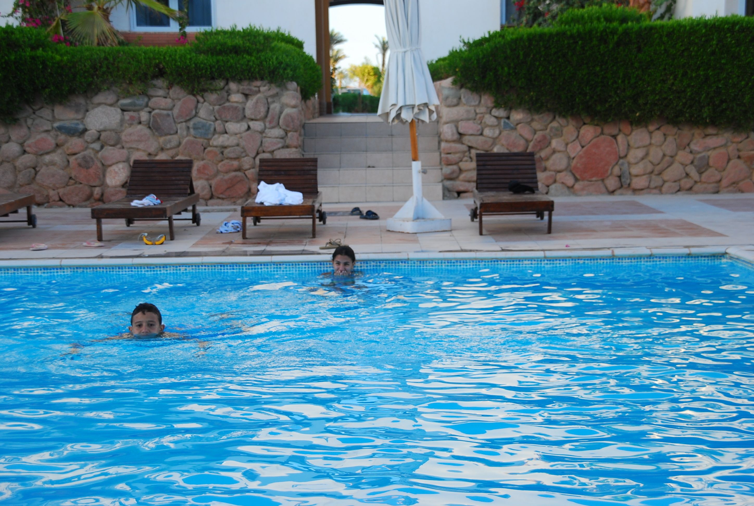 A swimming pool with lounge chairs and a stone wall.