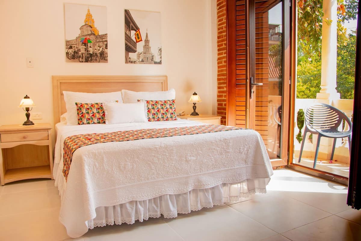 Une chambre à coucher avec un lit, deux tables de chevet, une fenêtre donnant sur un beau paysage et une chaise à l’extérieur.