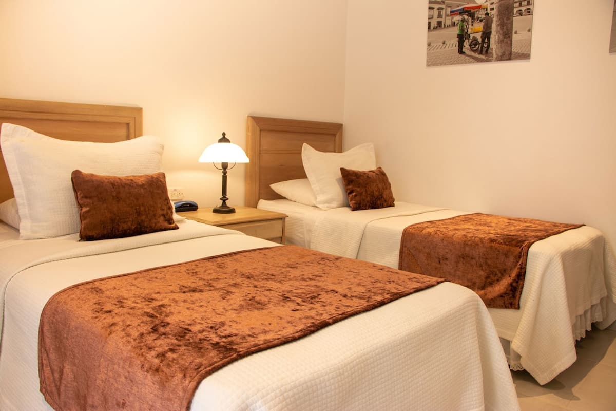Une chambre d’hôtel avec deux lits, chacun doté d’une tête de lit marron, d’une table de chevet avec une lampe et d’un tableau accroché au mur.