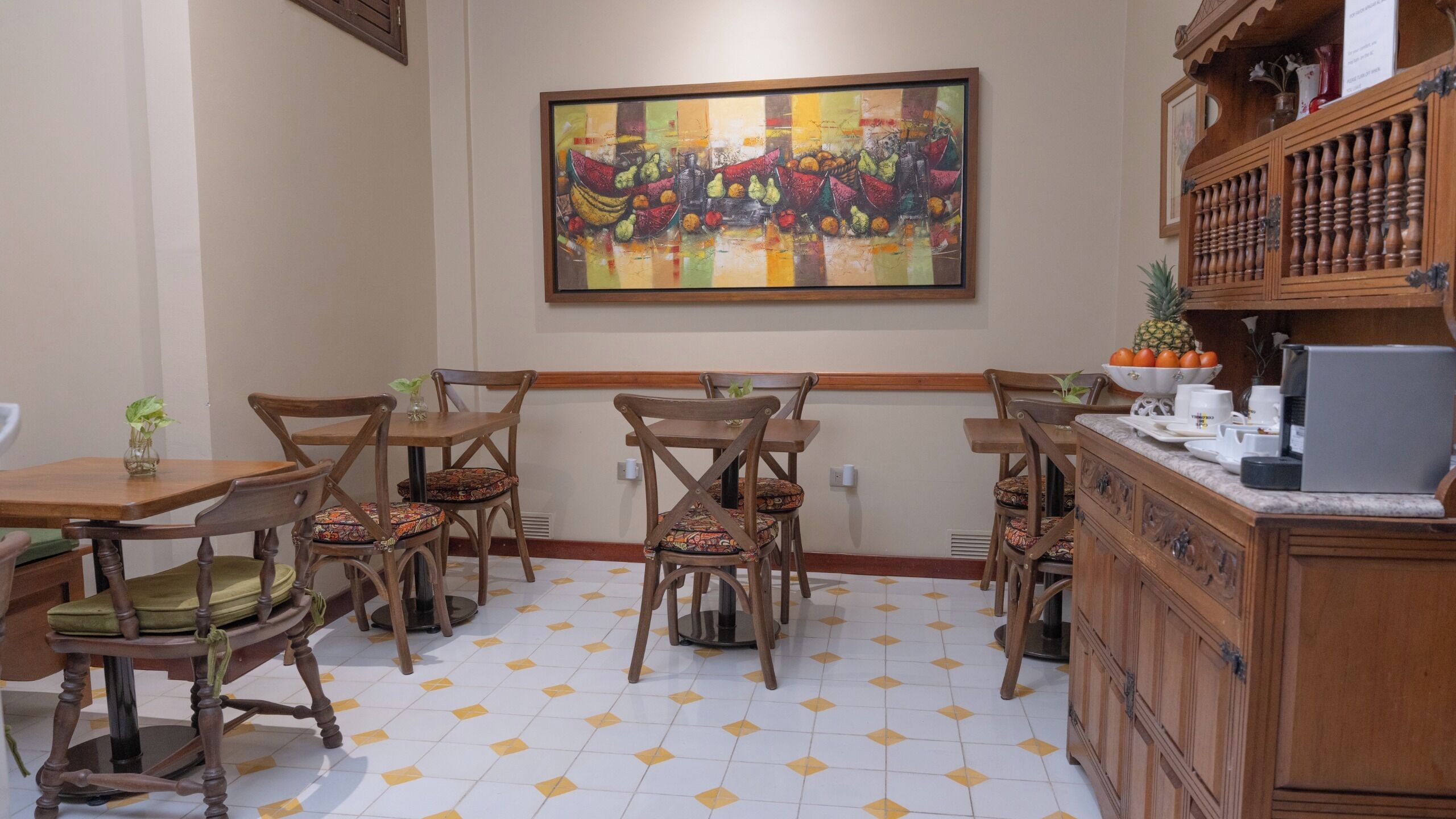 A dining area with wooden tables and chairs, a tiled floor, and a painting on the wall.