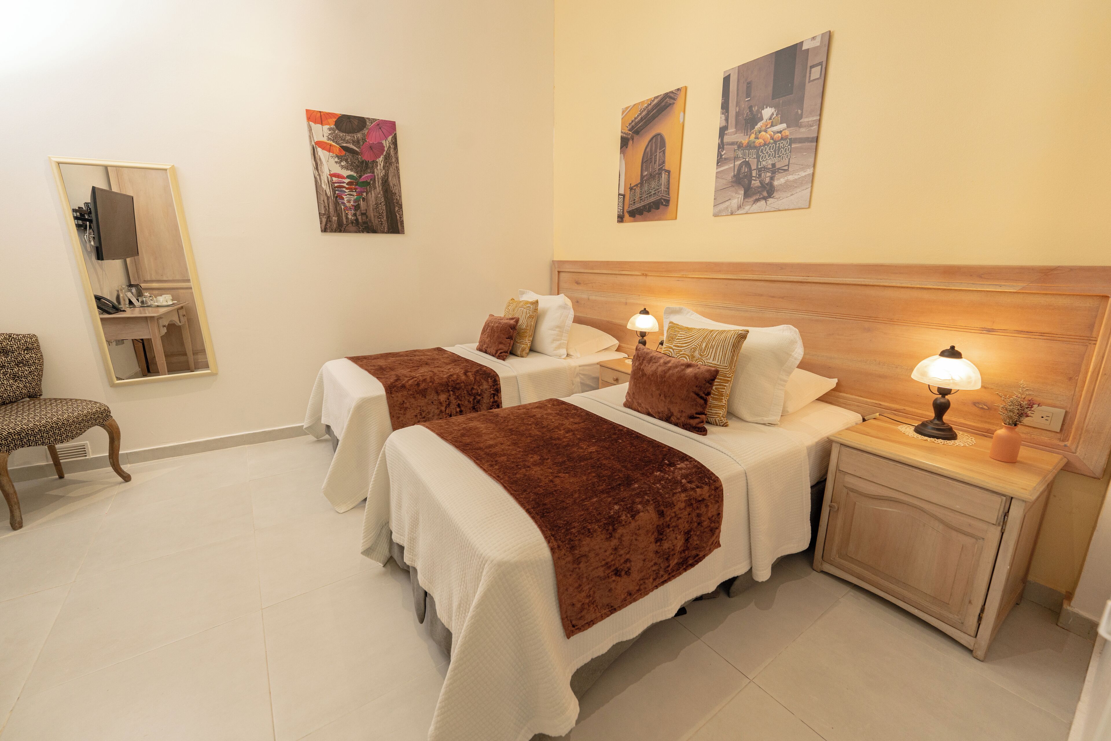 A hotel room with two beds, a desk, a chair, and artwork on the walls.