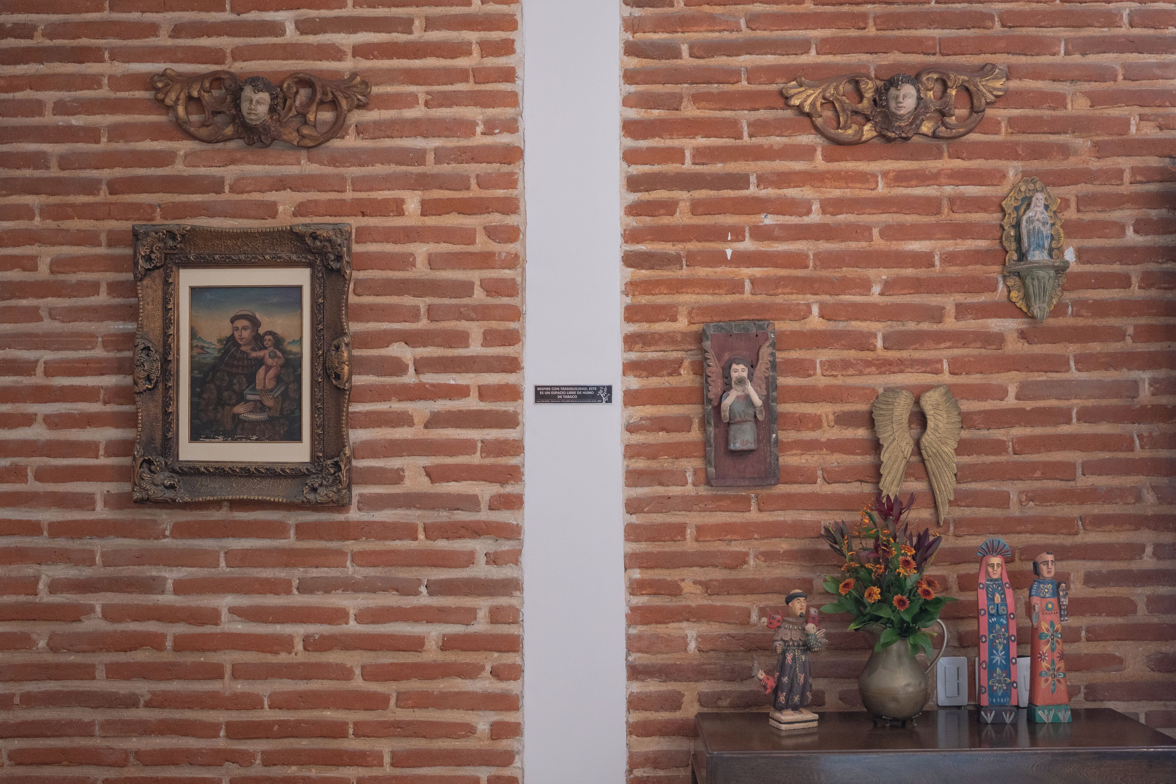 A brick wall with a framed picture, a small plaque, and decorative items including a vase with flowers and figurines.