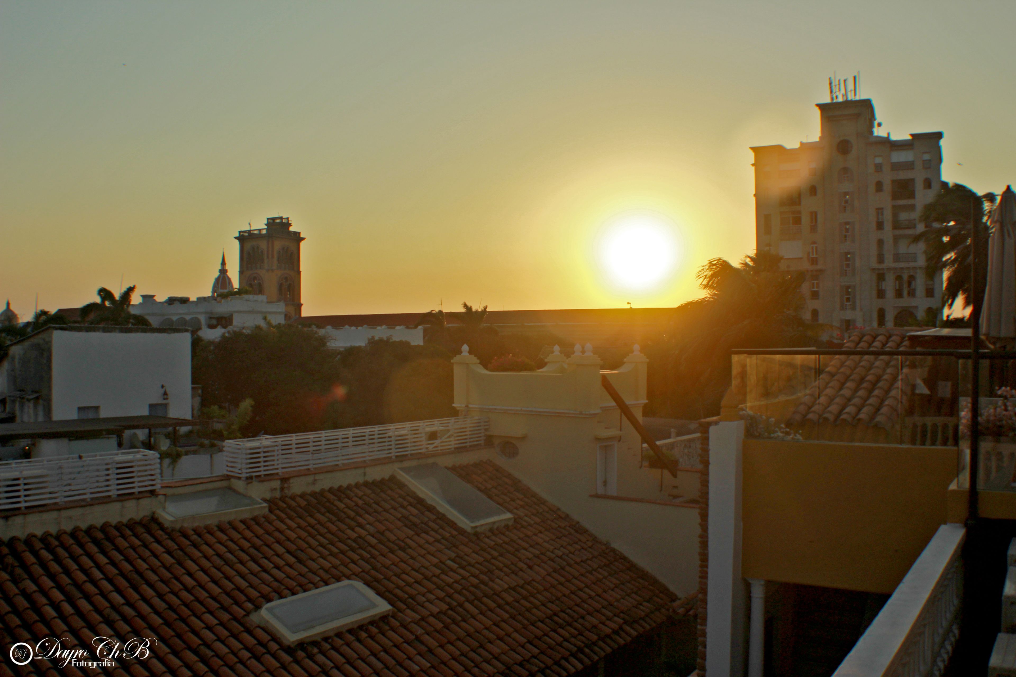 Eine Dachterrasse mit Blick auf den Sonnenuntergang und ein Gebäude mit einem Glockenturm.