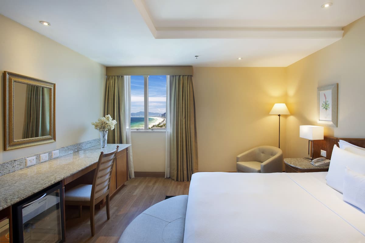 Habitación de hotel con cama, escritorio, silla y vista a la playa.