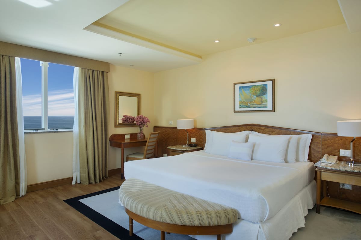 Una habitación de hotel con una cama grande, un escritorio, una silla, una ventana con cortinas y un cuadro en la pared.