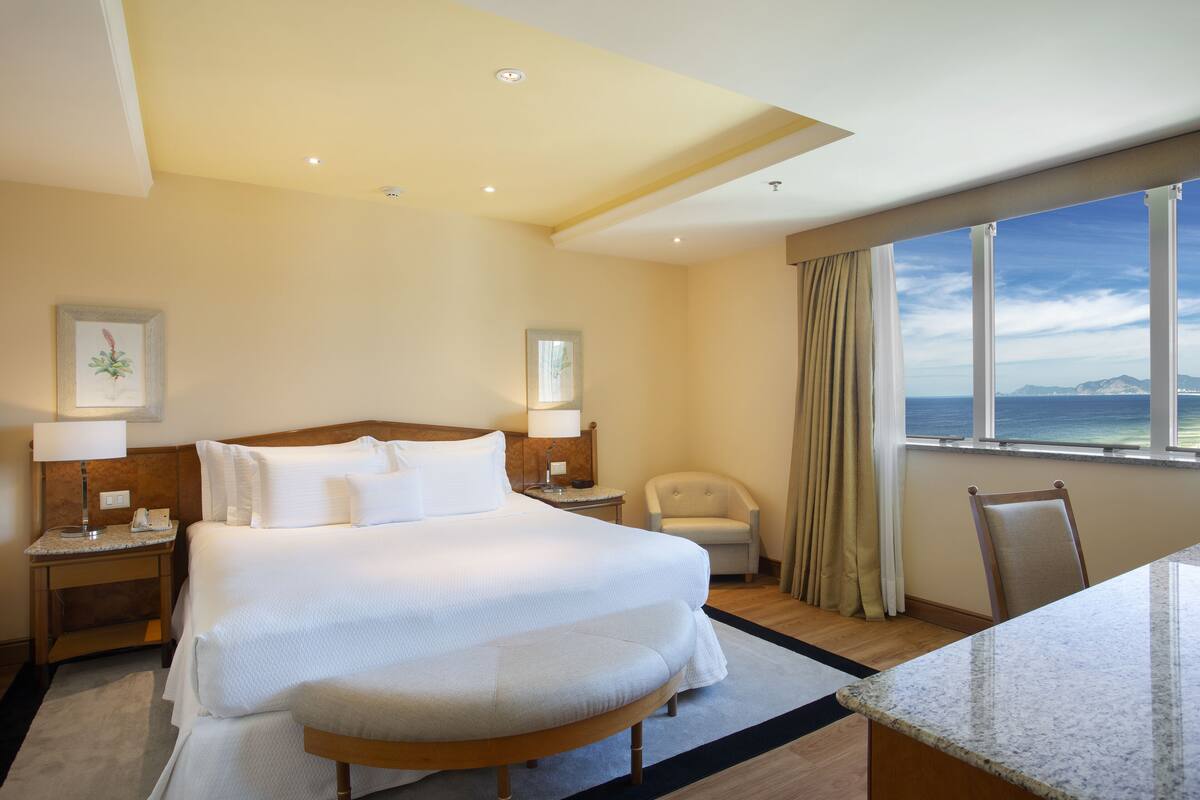 Habitación de hotel con una cama grande, un escritorio, una silla y vista al océano.