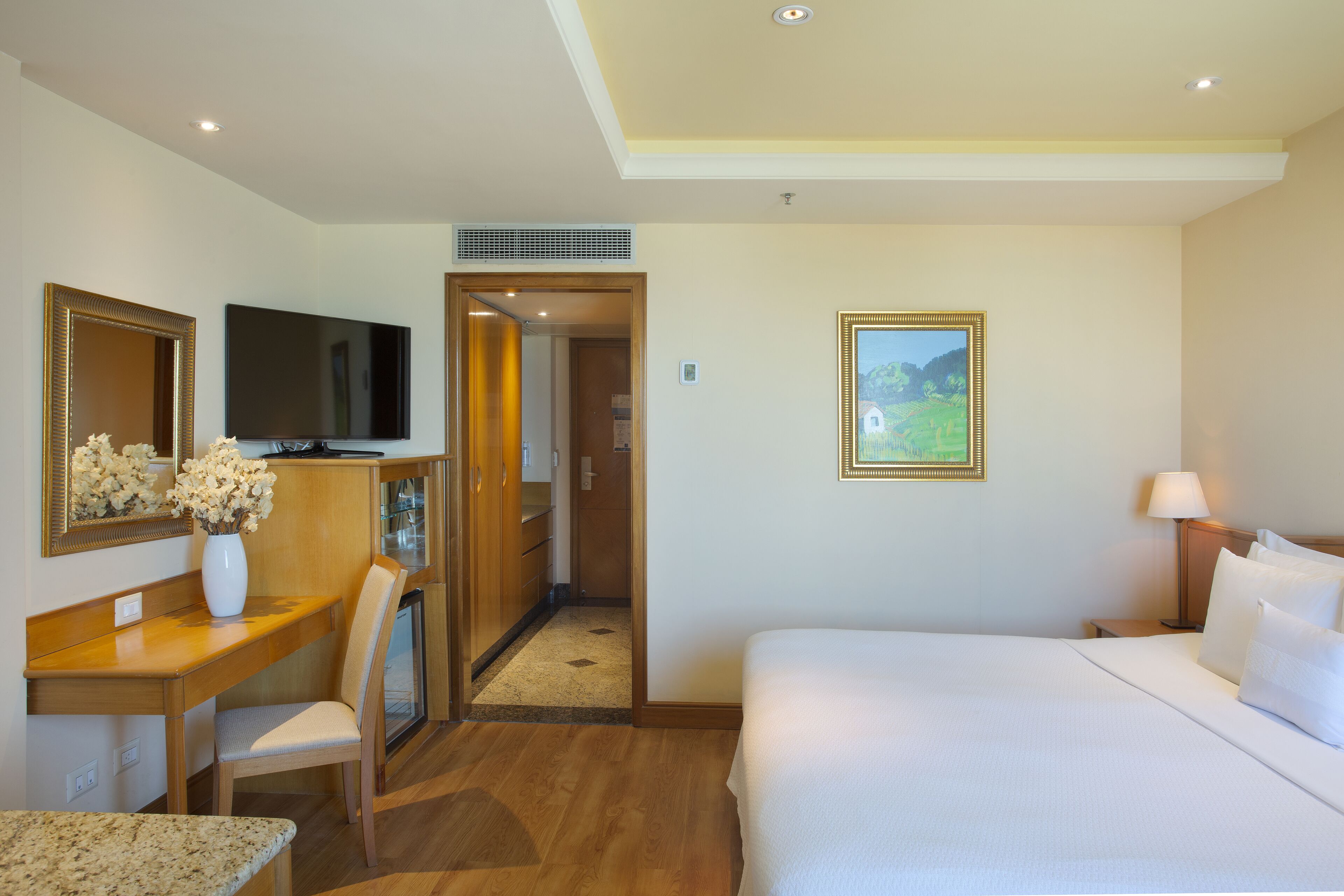 Ein Hotelzimmer mit Bett, Schreibtisch, Stuhl, Fernseher und einem Bild an der Wand.