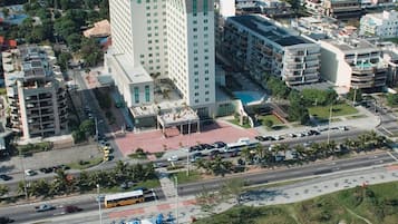 An aerial view of a coastal city with a prominent hotel featuring multiple floors, a beach, and surrounding urban development.
