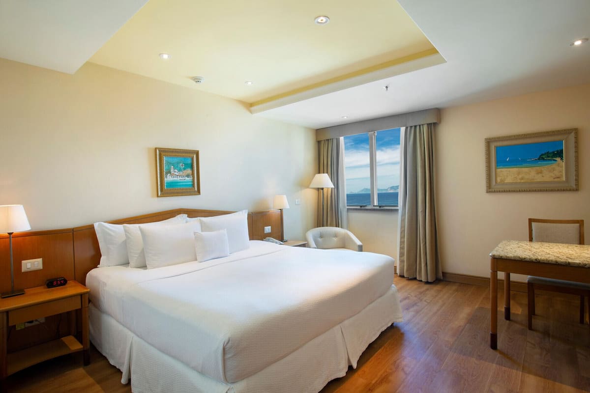 Habitación de hotel con una cama grande, un escritorio, una silla, una ventana con vistas y un cuadro en la pared.