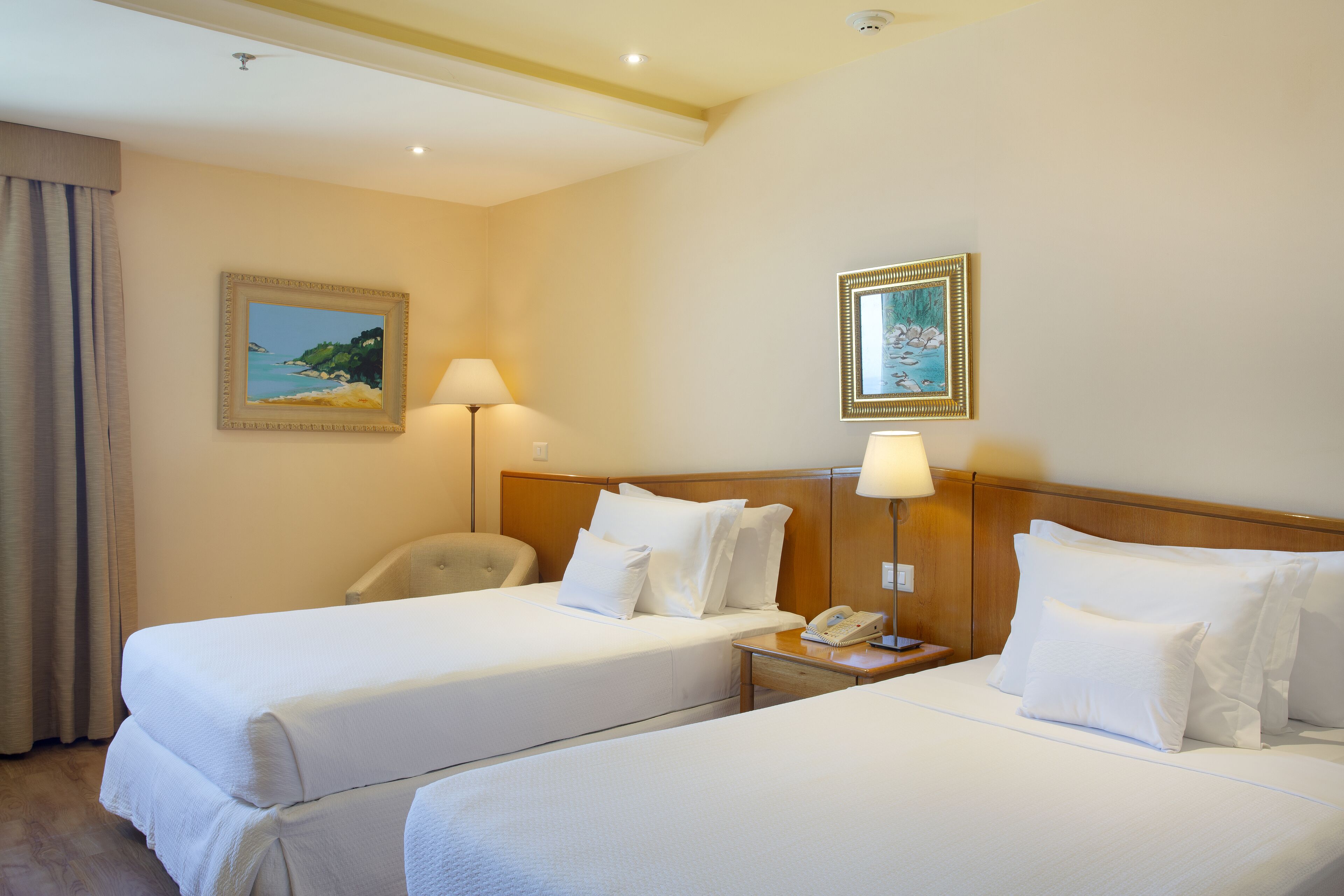 Une chambre d’hôtel avec deux lits, une table de chevet, une lampe et un tableau au mur.