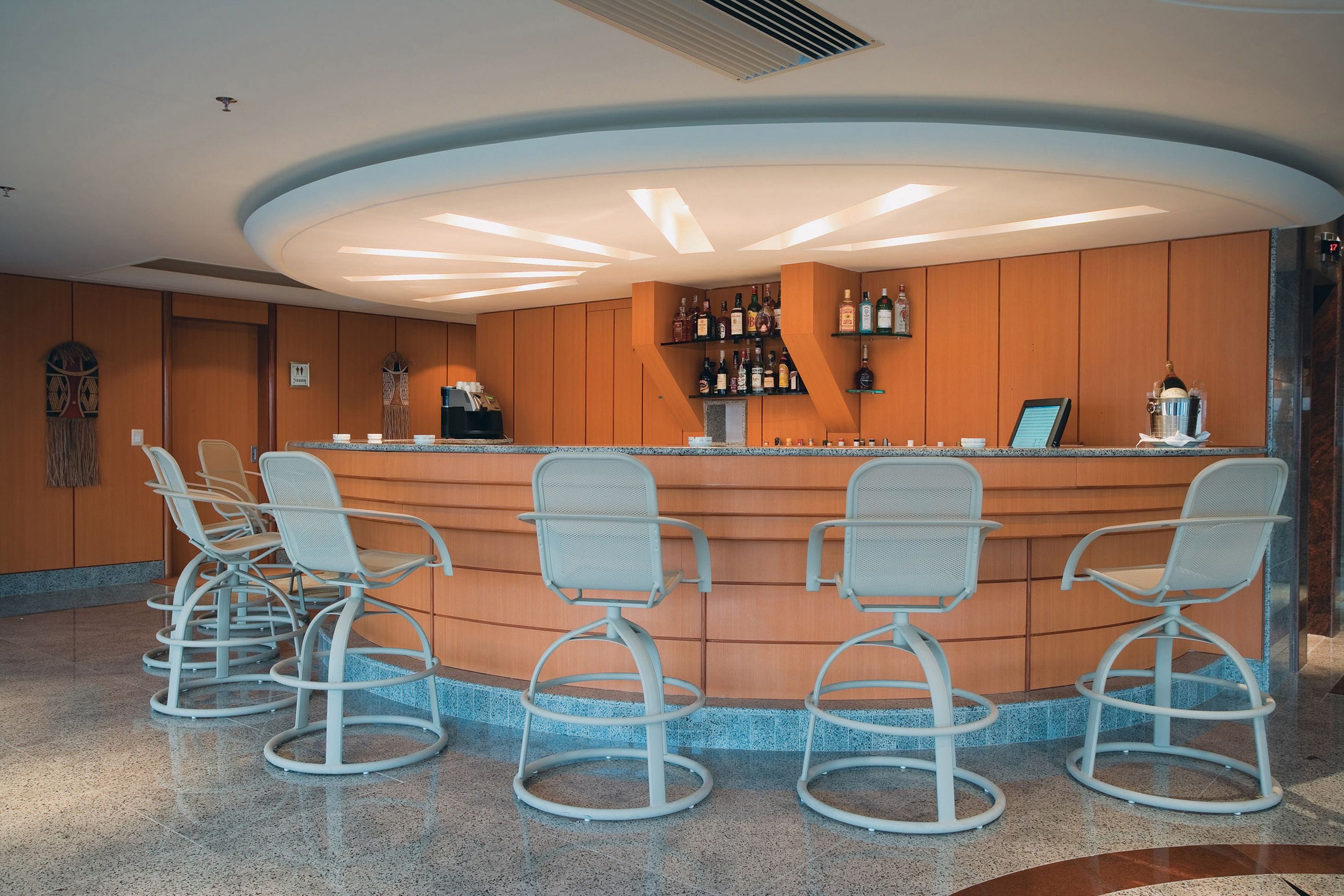 A bar area with a curved counter, four bar stools, and a selection of bottles on shelves.