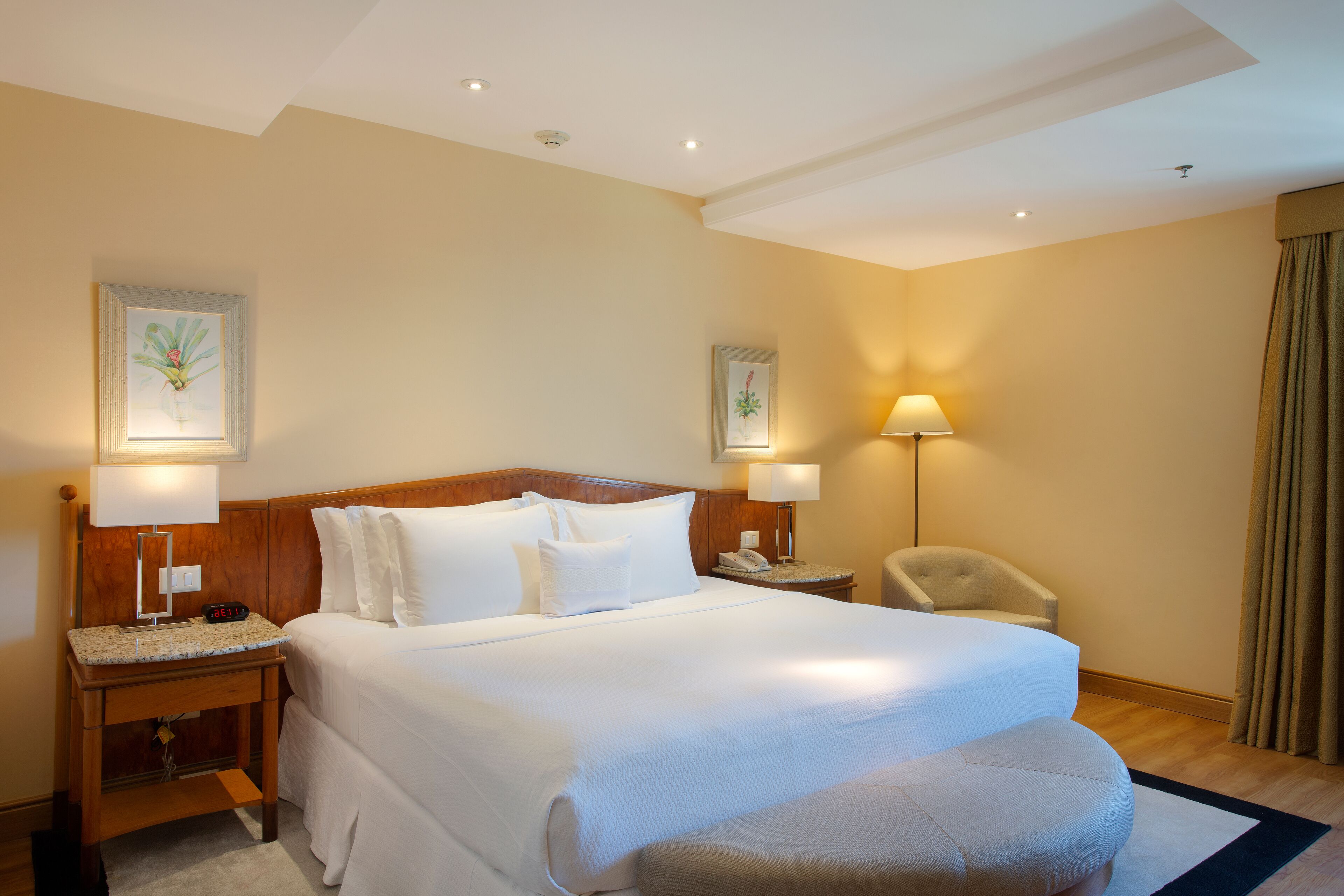 A hotel room with a large bed, two bedside tables with lamps, a chair, and artwork on the walls.