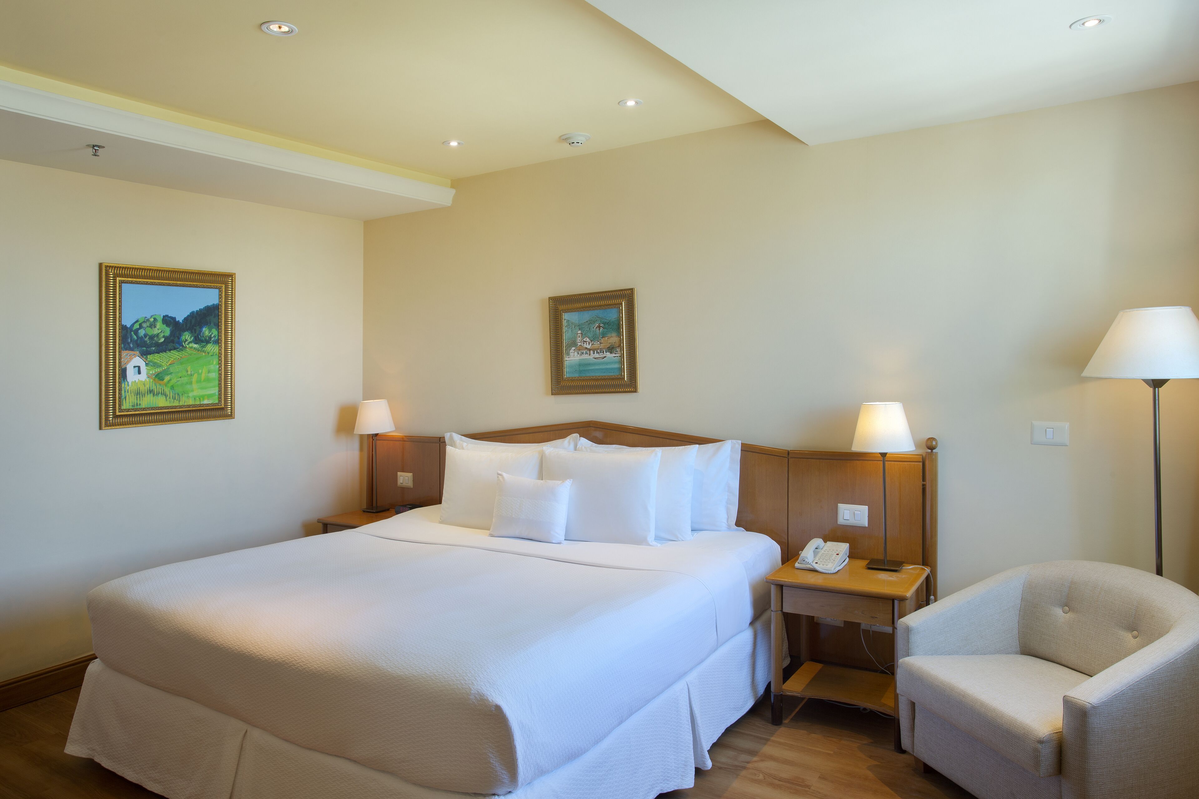Ein Hotelzimmer mit einem großen Bett, zwei Nachttischen mit Lampen, einem Sessel und zwei gerahmten Bildern an der Wand.