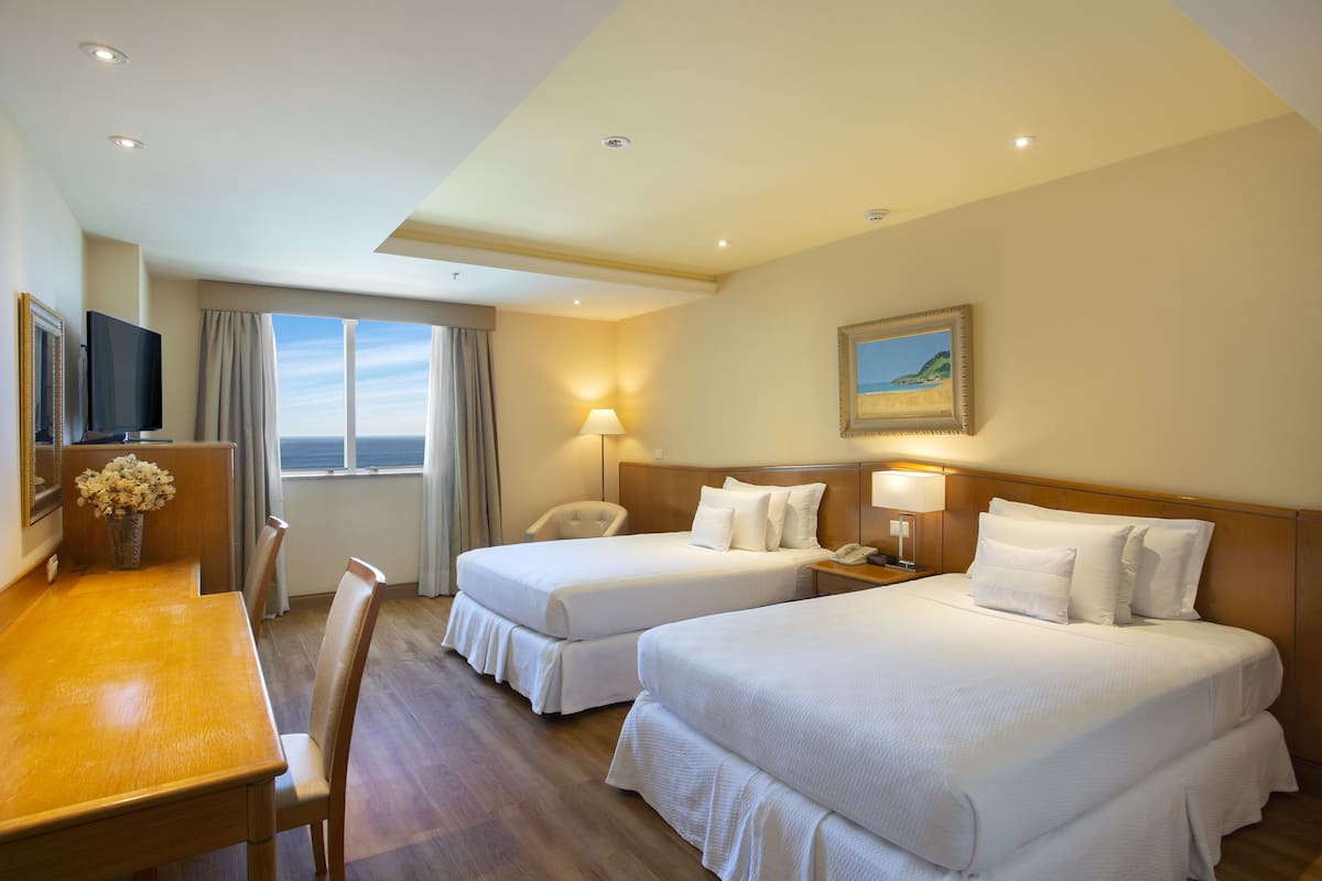Habitación de hotel con dos camas, un escritorio, una silla, un televisor y una ventana con vistas.
