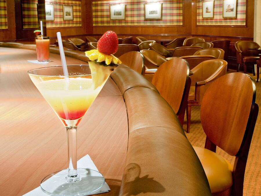 Un vestíbulo de hotel con un sofá de cuero largo, una zona de bar con una bebida y cuadros enmarcados en la pared.