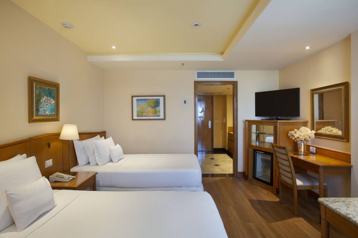 Habitación de hotel con dos camas, un escritorio con silla, televisión y refrigerador pequeño.