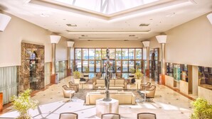 A spacious lobby with a high ceiling, large windows, and a central seating area with sofas and tables.