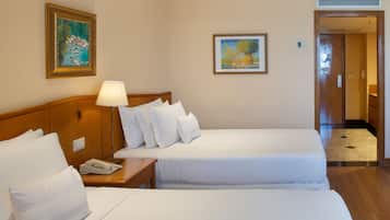 Una habitación de hotel con dos camas, una mesita de noche con lámpara y obras de arte en las paredes.