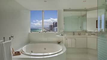 A modern bathroom with a large bathtub, a glass shower enclosure, and a view of the ocean and city skyline.
