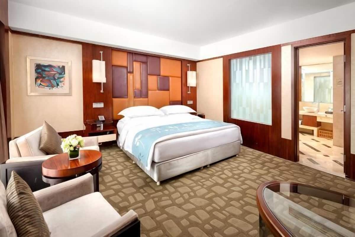 Een hotelkamer met een bed, een zithoek met een stoel en een tafel, een nachtkastje en een groot raam.