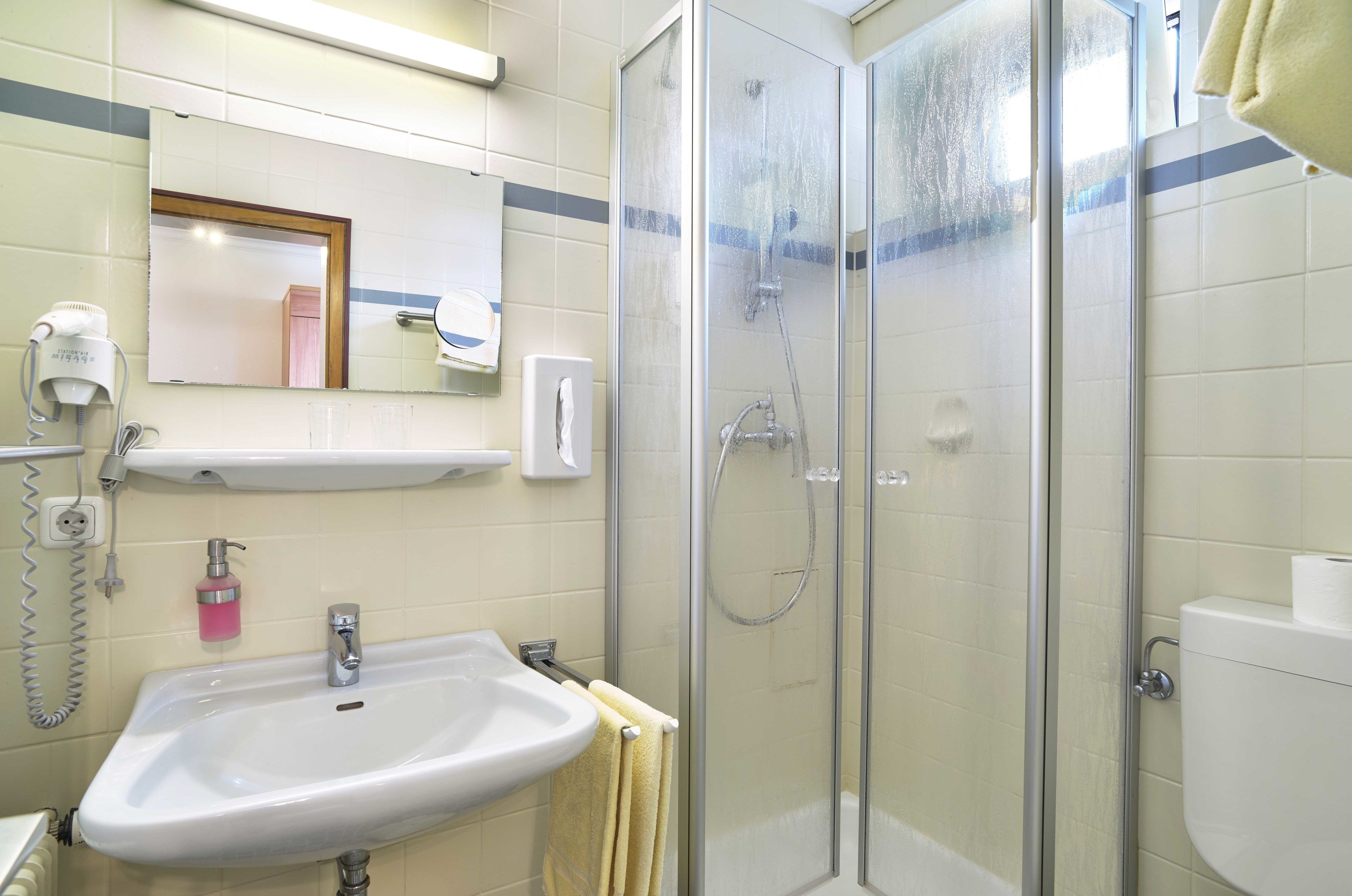 A bathroom with a sink, mirror, towel rack, and glass-enclosed shower.