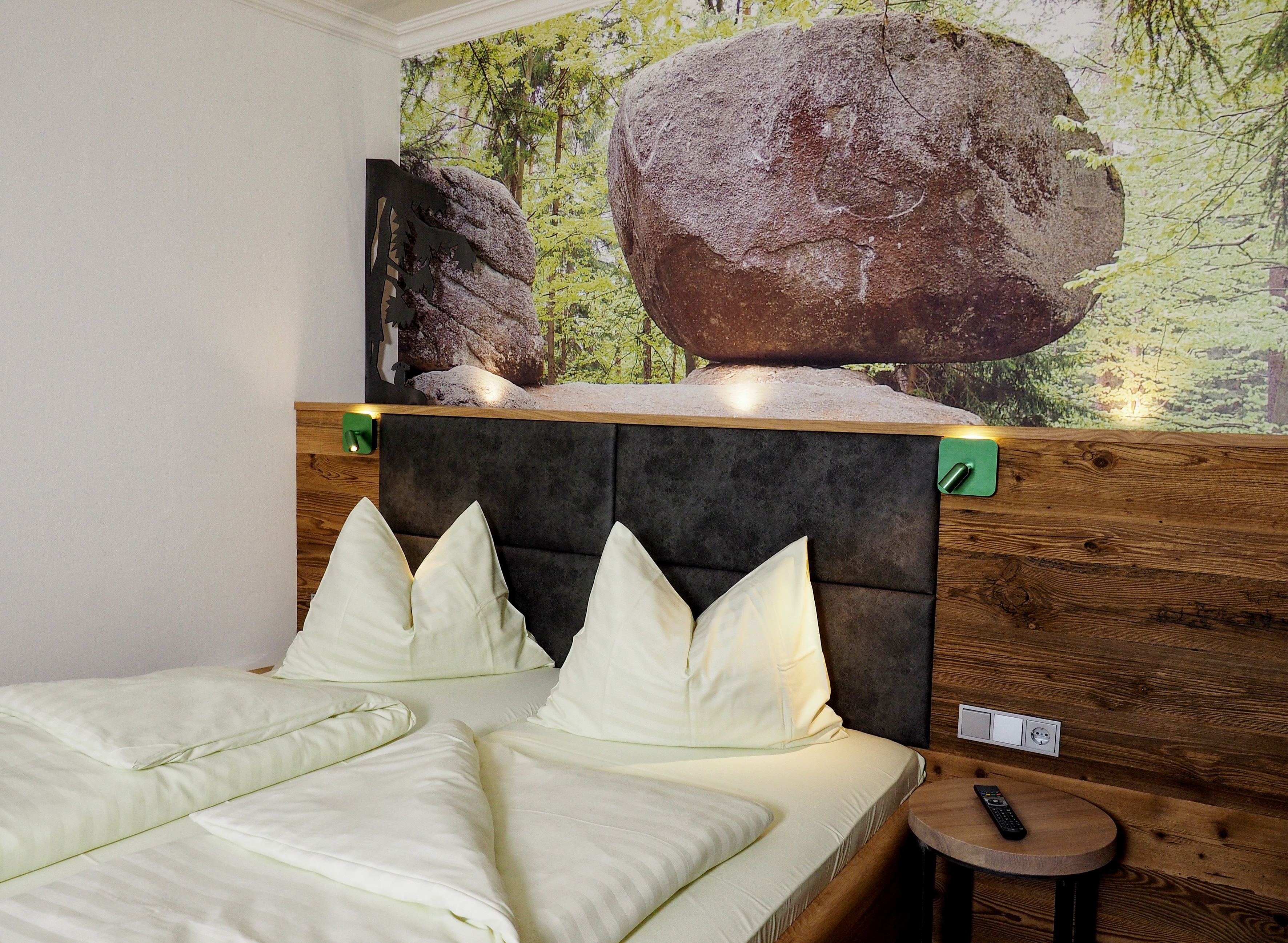 A bedroom with a bed, pillows, a headboard, a wall-mounted TV, and a wooden side table.
