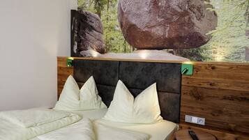 A bedroom with a bed, pillows, a headboard, a wall-mounted TV, and a wooden side table.