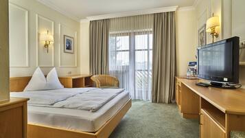 Habitación de hotel con una cama grande, un escritorio con televisión, una silla y una ventana con cortinas.