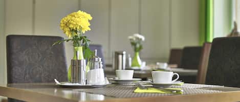 A dining table set with a vase of yellow flowers, white cups, and a green vase.