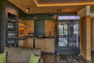 Una cocina moderna con armarios de madera, una zona de bar con estantes llenos de vasos y un refrigerador grande repleto de bebidas.