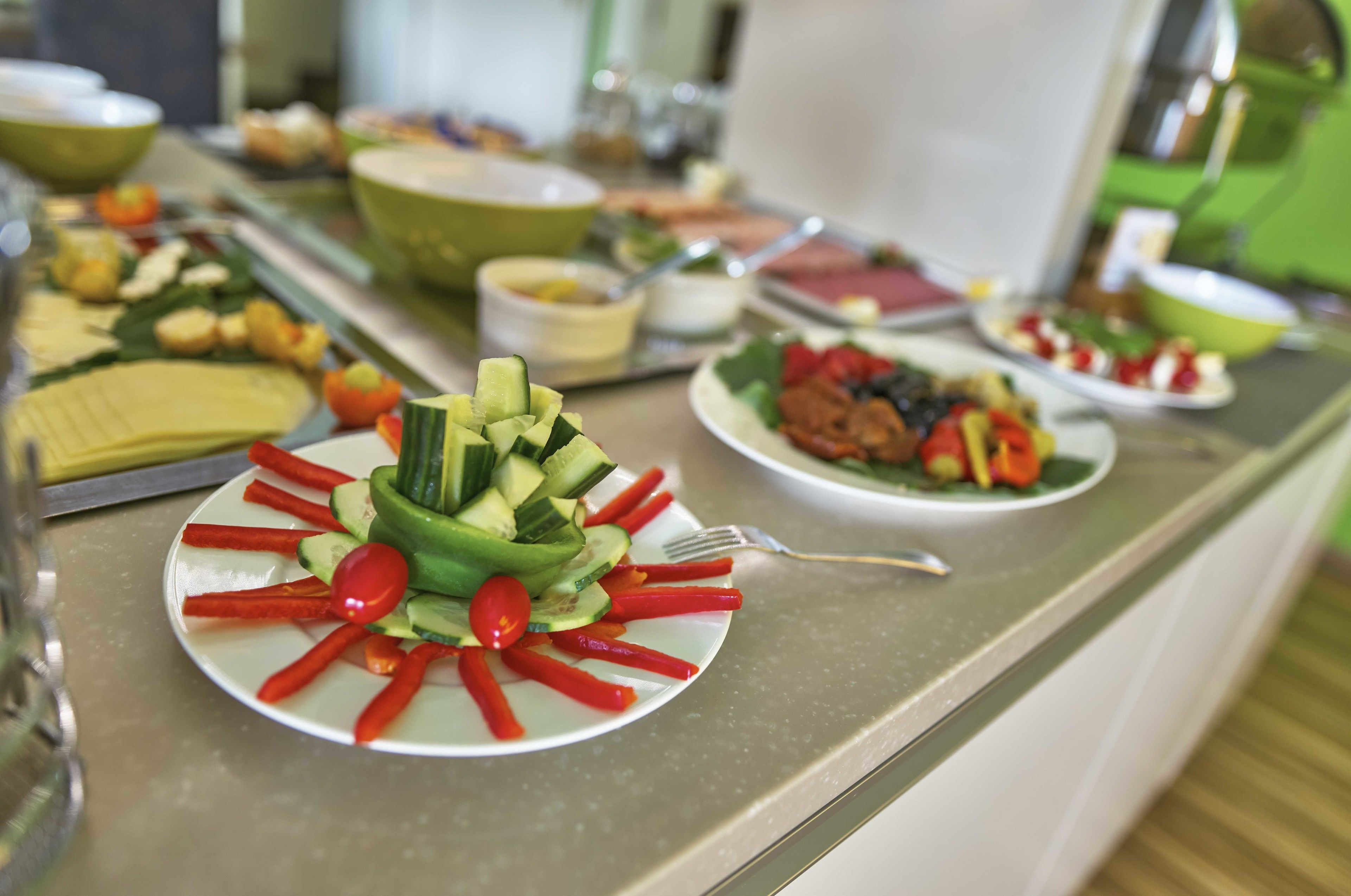 A buffet table with various dishes, including a salad with cucumbers, tomatoes, and red peppers.