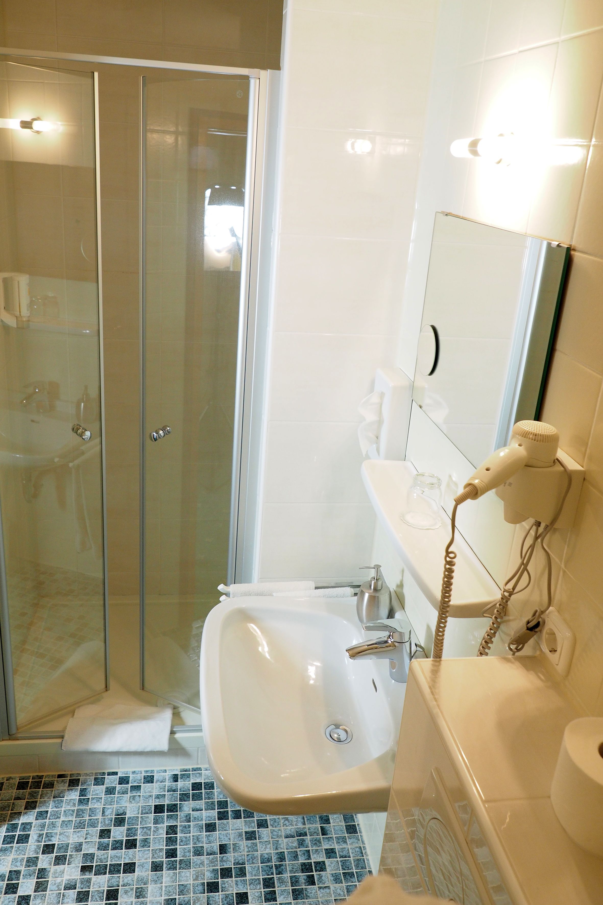 A bathroom with a glass shower enclosure, a sink, and a hairdryer mounted on the wall.