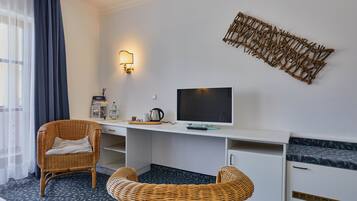 Habitació d'hotel amb llit, escriptori amb televisió, cadires de vímet, làmpada penjada a la paret i un element decoratiu a la paret.
