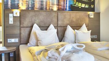 A hotel room with a large bed, a headboard with a cityscape mural, a bedside table, and a flat-screen TV mounted on the wall.