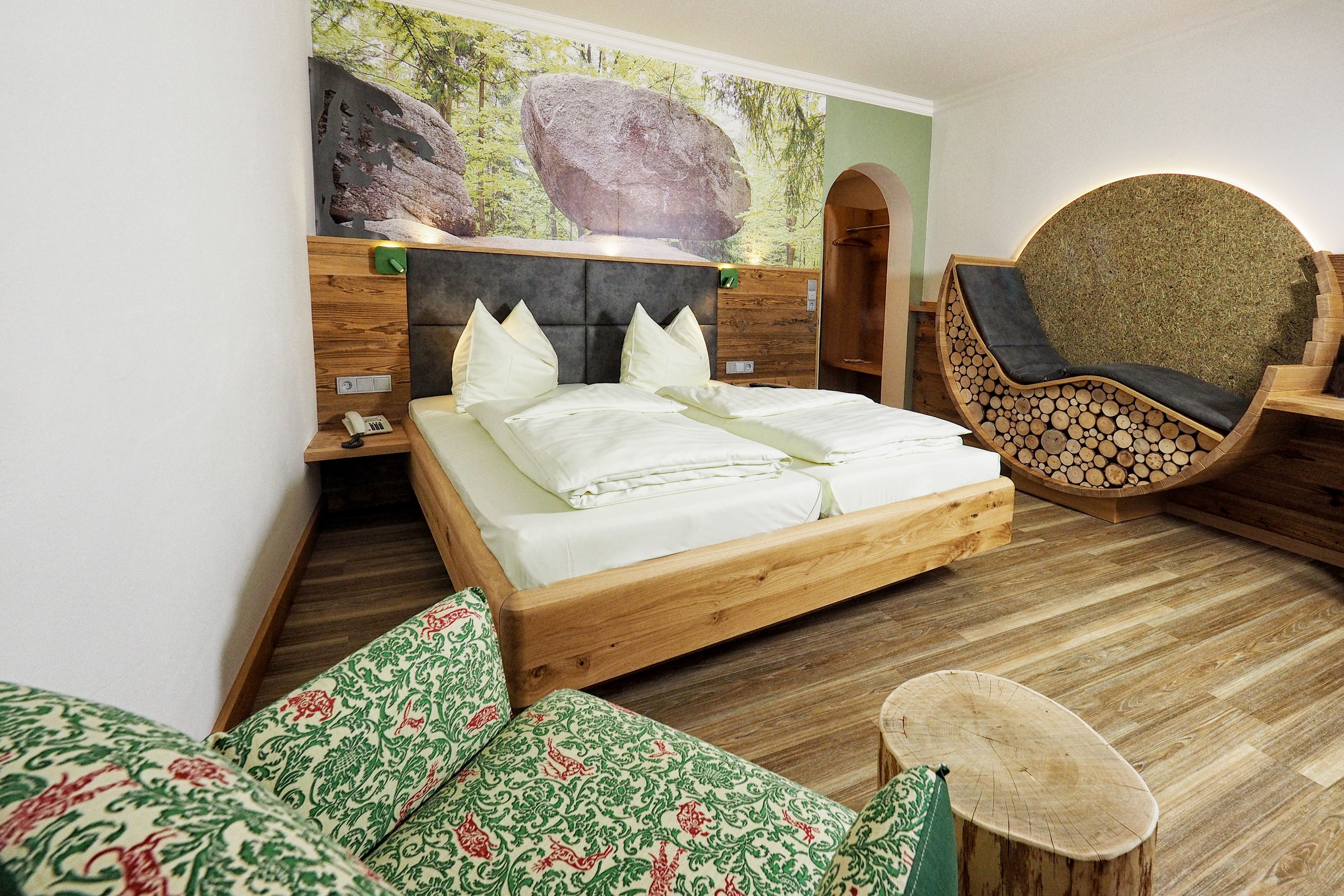A modern bedroom with a wooden bed, a large wall mural, a unique circular chair, and a small wooden stool.