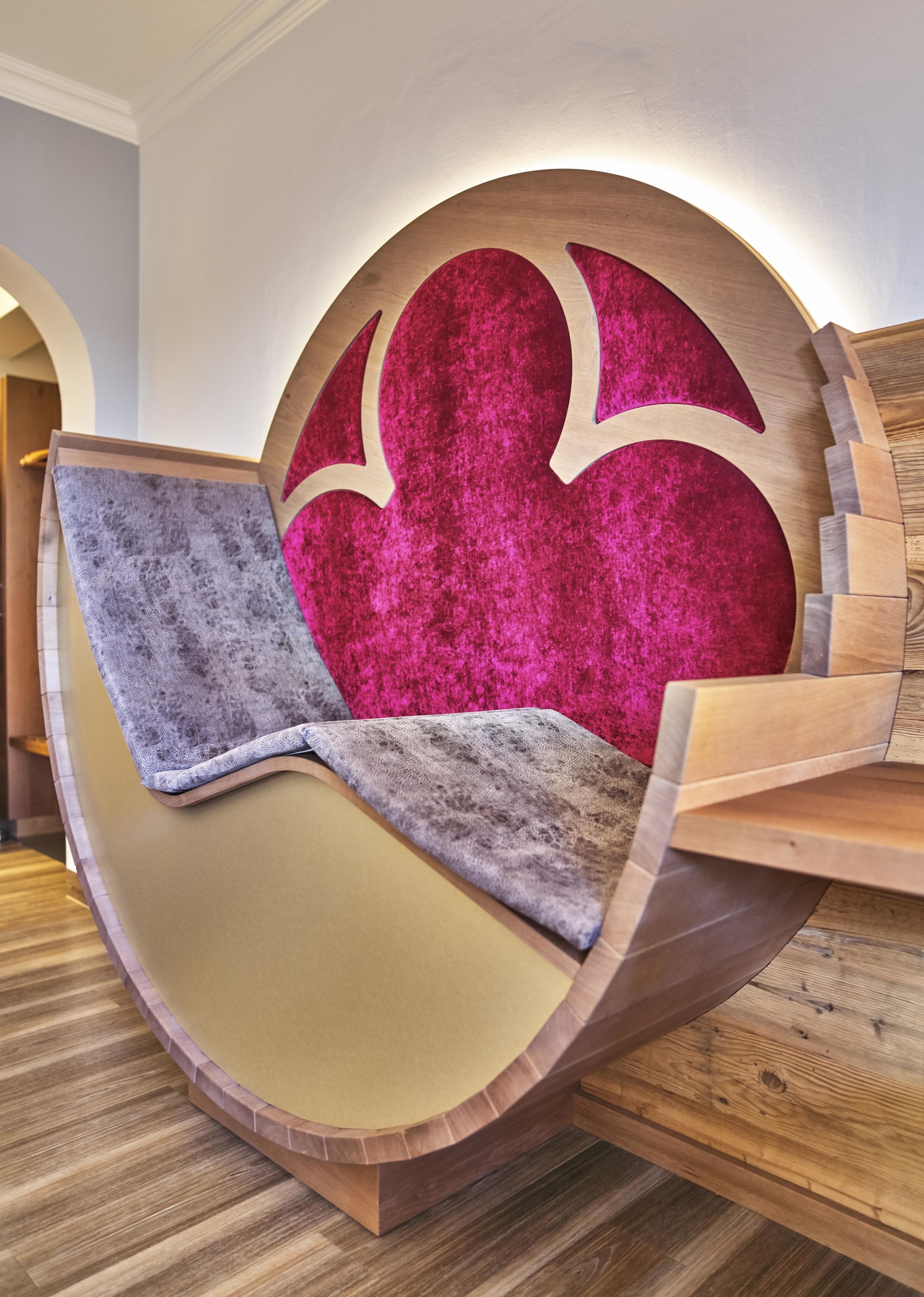Una silla de madera con forma original, con un cojín rosa intenso y una manta gris.