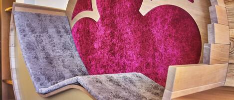 Una silla de madera con forma original, con un cojín rosa intenso y una manta gris.