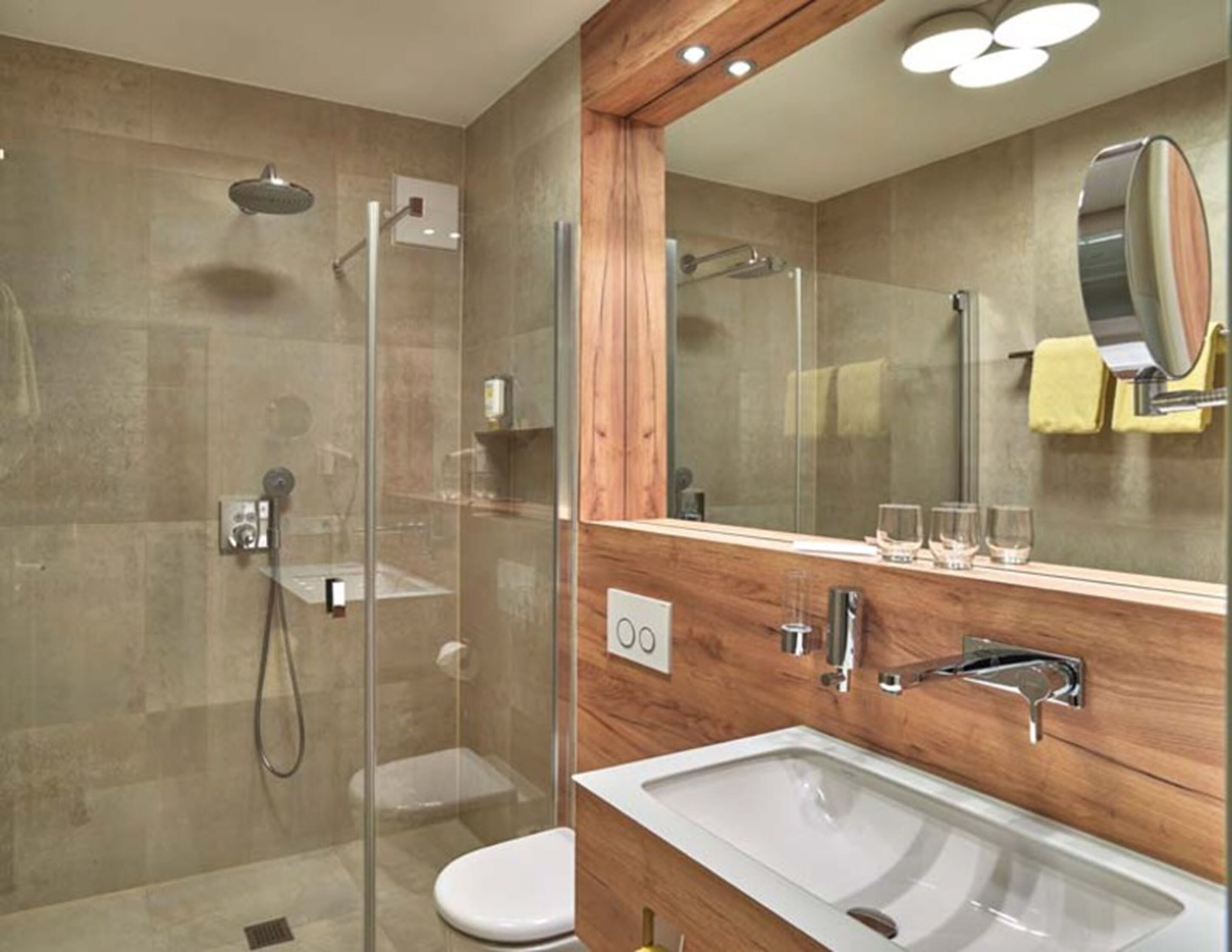 Un baño moderno con ducha de vidrio, tocador de madera con lavamanos y un espejo grande.
