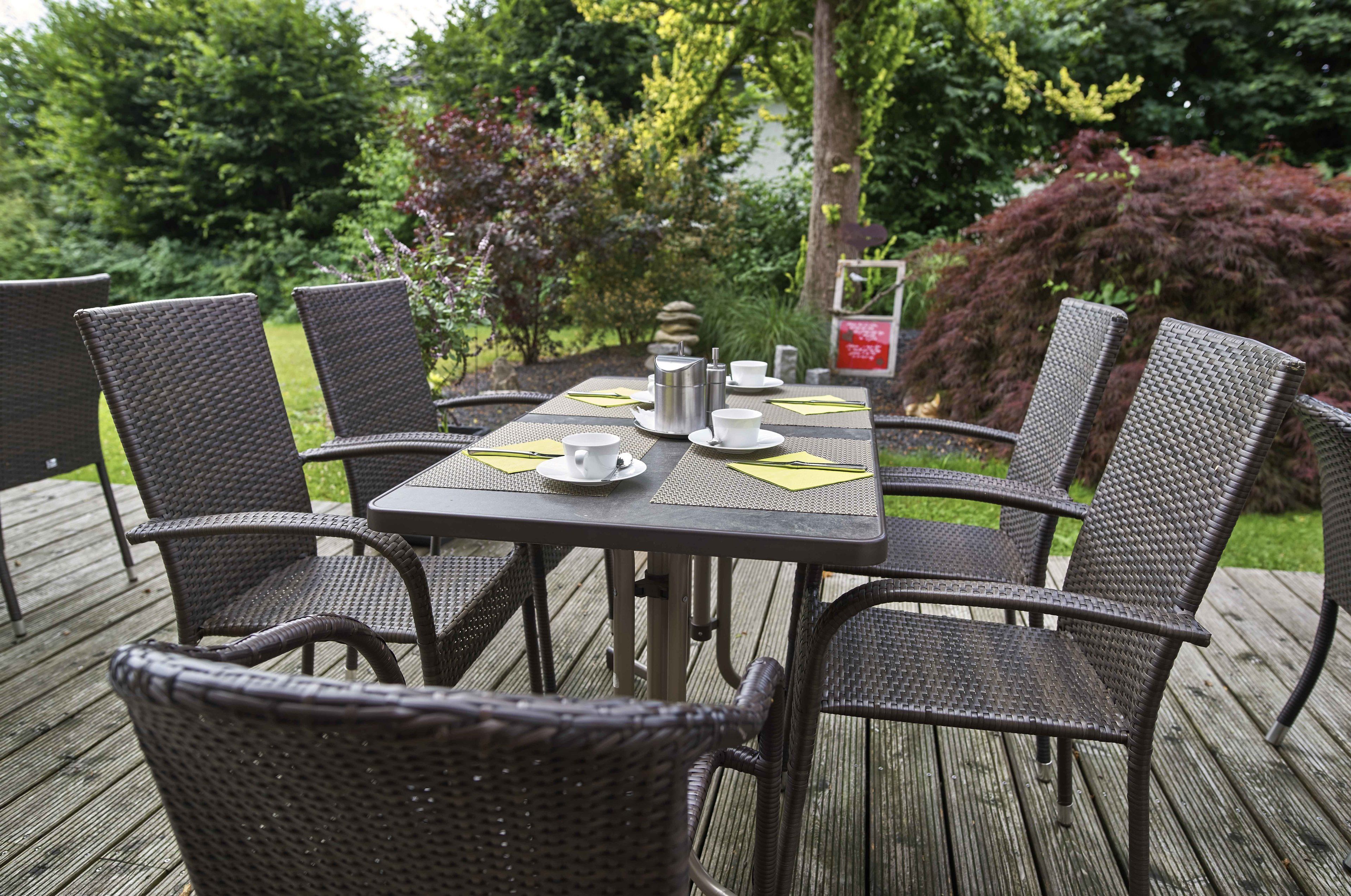 A wooden deck with a table set for four, surrounded by wicker chairs.