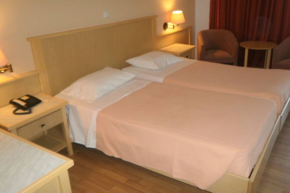 A hotel room with two beds, a nightstand, a chair, and a small table.