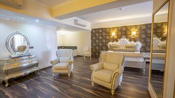 A hotel room with a large bed, a vanity with a mirror, two armchairs, and a dresser.