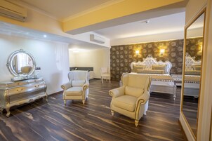 A hotel room with a large bed, a vanity with a mirror, two armchairs, and a dresser.